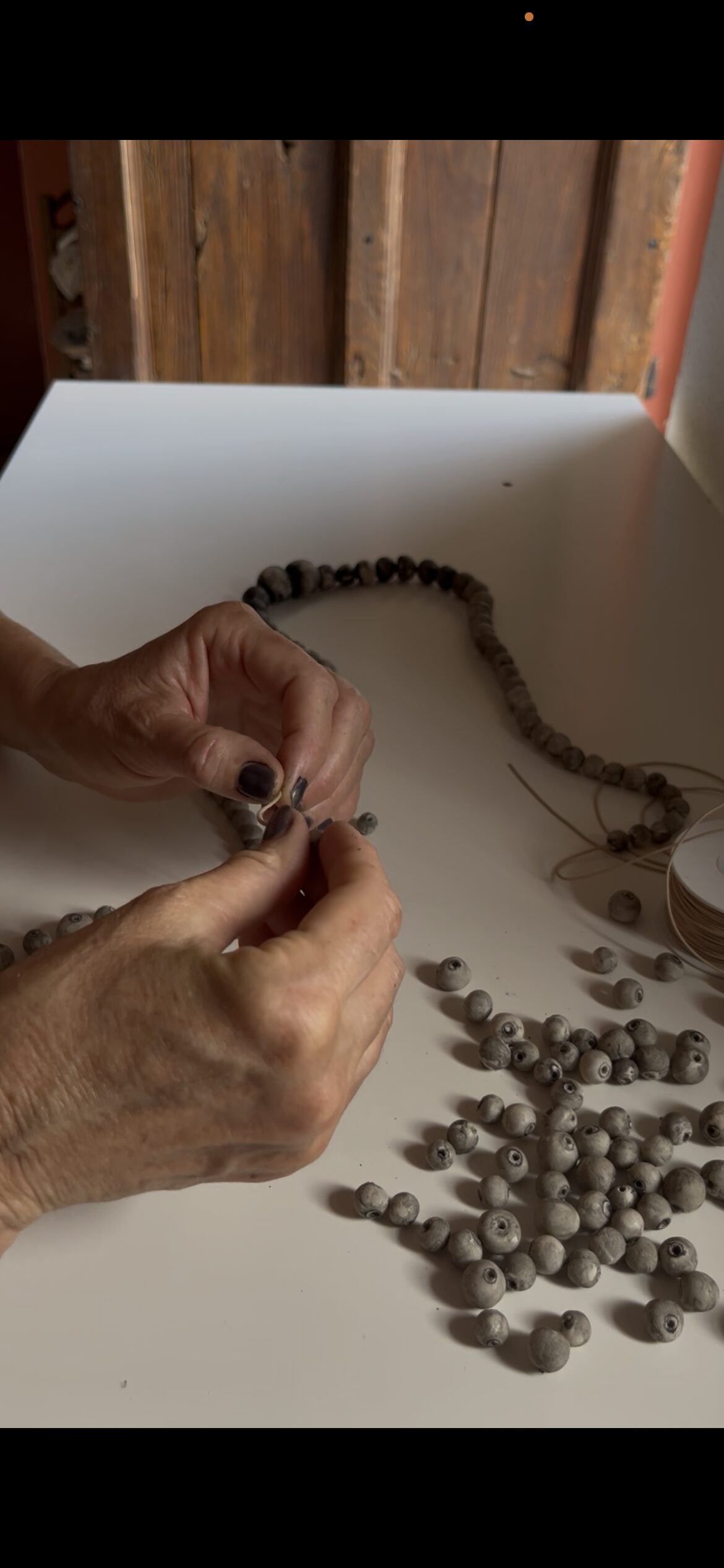 Hands threading handmade eggshell porcelain pearls by Italian contemporary jewelry artist Patrizia Giachero